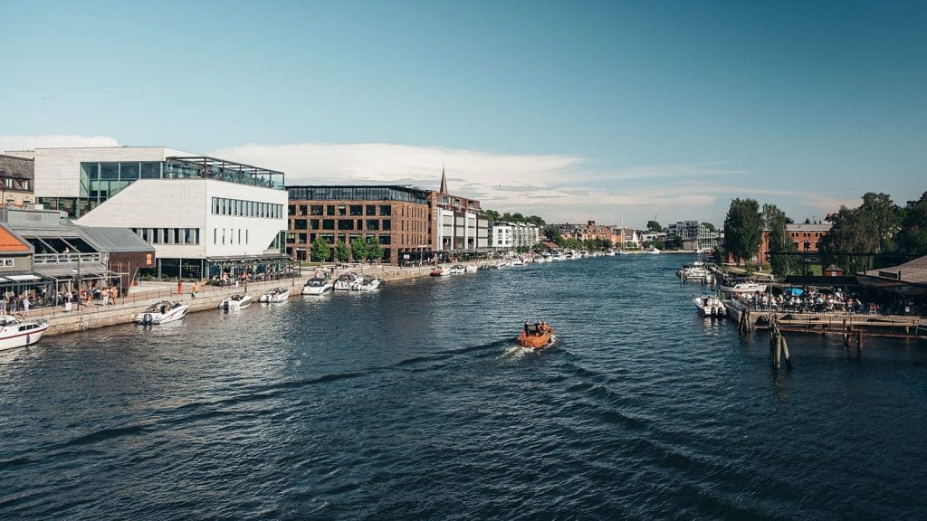 Bryggepromenaden i Fredrikstad sentrum med båter, moderne bygg og folk som nyter sommerdagen ved vannet.