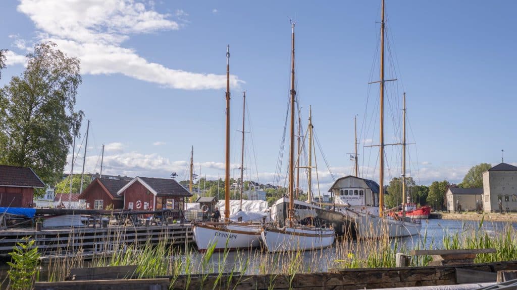Gamle trebåter og seilskuter ligger til kai ved røde sjøboder i Isegran i Fredrikstad.