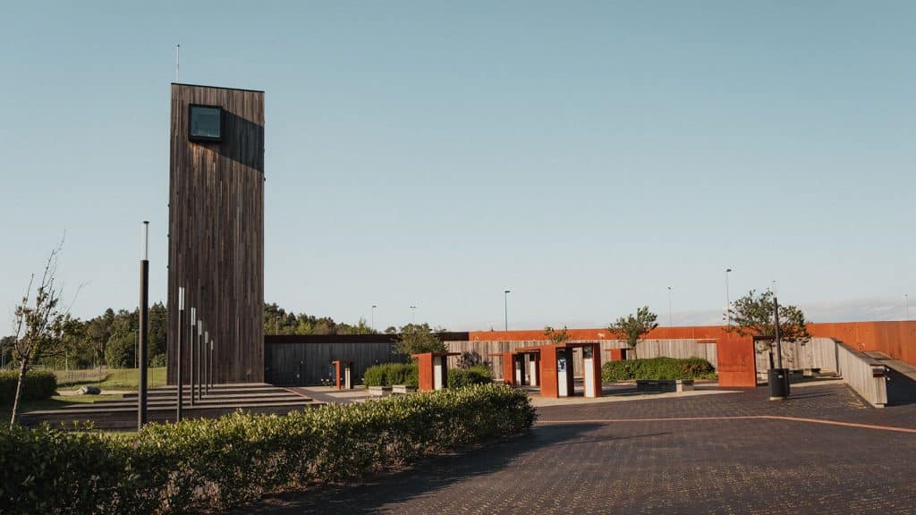 Solbergtårnet med tilhørende informasjonssenter i cortenstål og tre, omgitt av grønt landskap.