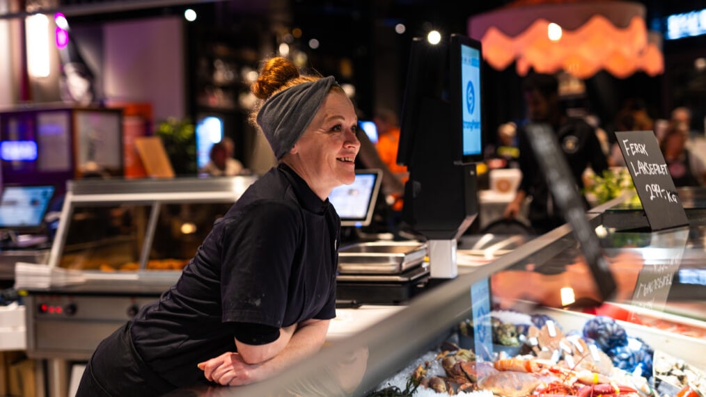 Ansatt smiler bak fiskedisken hos Gla’laksen på Matværste, med fersk sjømat i front