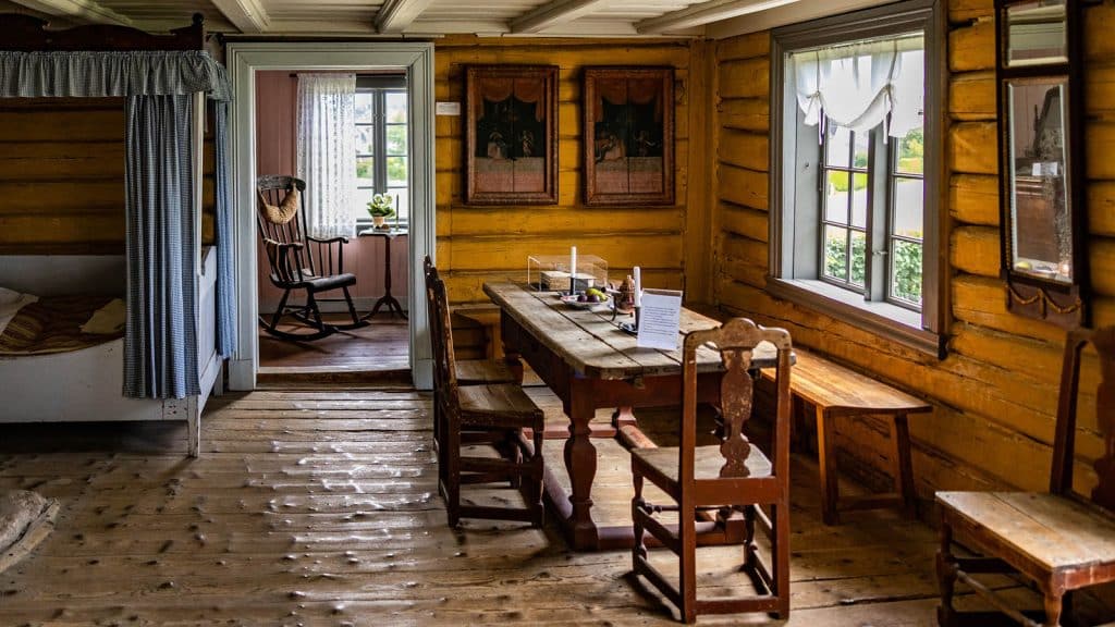 Tradisjonelt interiør fra Hans Nielsen Hauges barndomshjem på Rolvsøy, med trebenker, bord og seng.