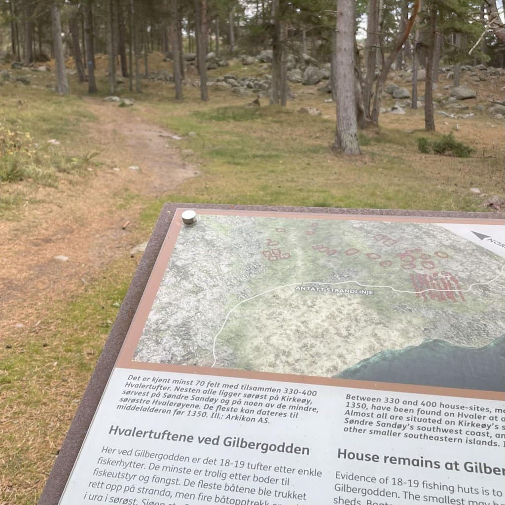 Informasjonsskilt om Hvalertuftene ved Gilbergodden, med skogssti i bakgrunnen.