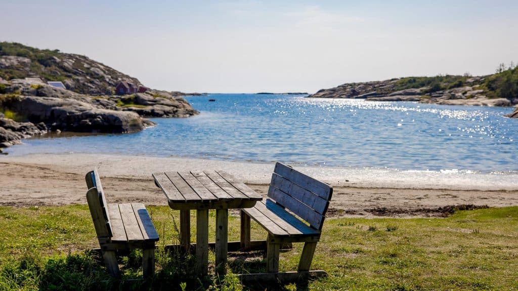 Rasteplass med bord og benk ved stranden i Kuvauen, med utsikt mot havet.