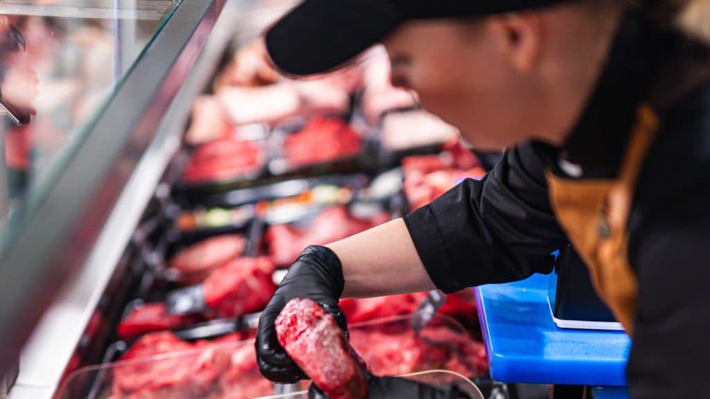Ansatt legger ut kjøtt i disk hos Manstad Kjøtt med stort utvalg av rødt kjøtt og tomahawk