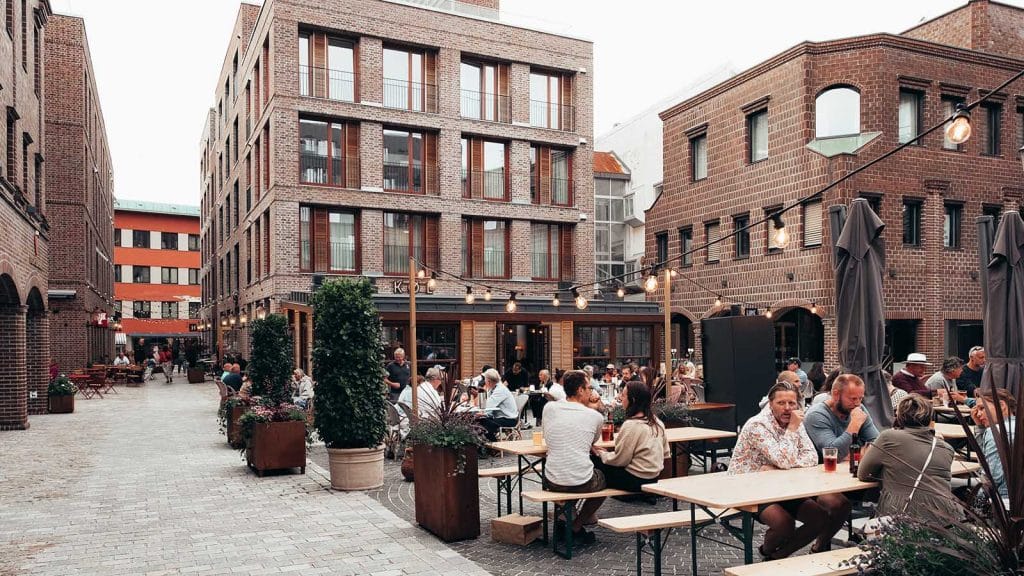 Moderne byrom med folk, matservering og mursteinshus på Nygaardsplassen i Fredrikstad