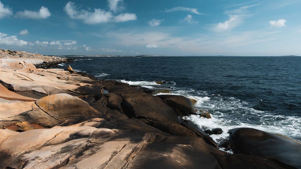 Glattskurte svaberg ved havet på Rødshue med bølger som slår mot land.