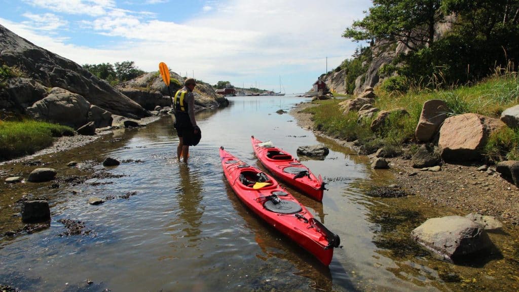 En person drar kajakken sin til land ved et smalt sund omgitt av svaberg.