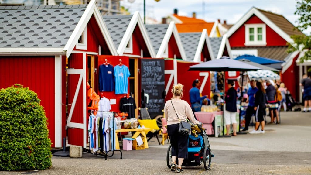 Person med barnevogn går mellom boder på torget med salg av klær og lokalvarer.