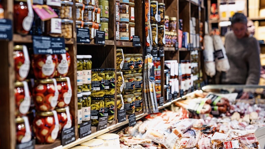 Delikatessebutikk med ost og oliven i disken og hyller fulle av europeiske spesialiteter.