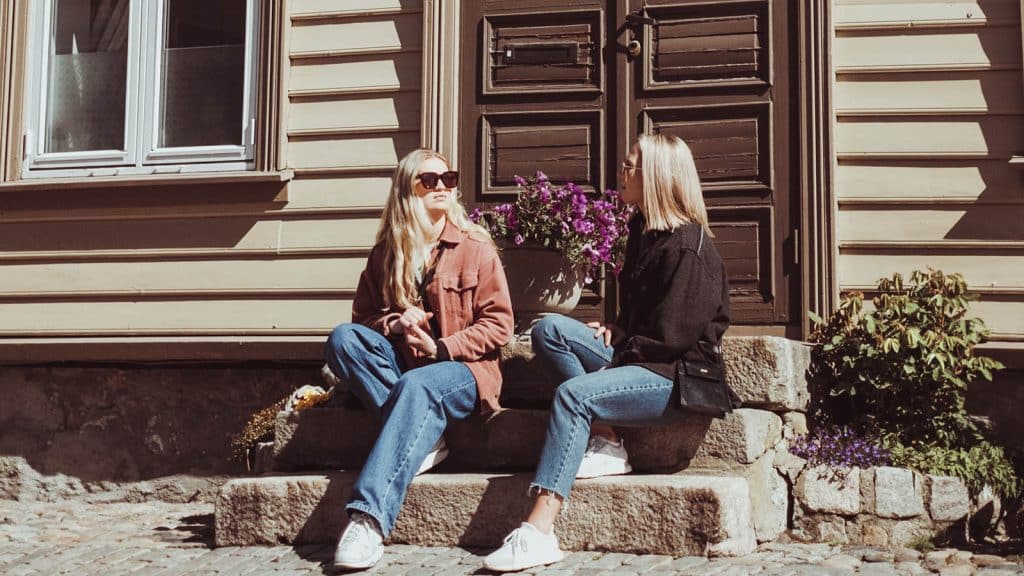 To unge kvinner sitter i sola på en trapp i Gamlebyen i Fredrikstad.