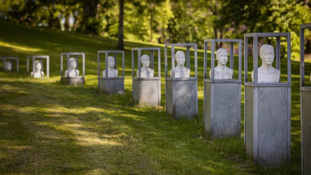 Rekke av hvite byster i rammer på sokler i en grønn park.