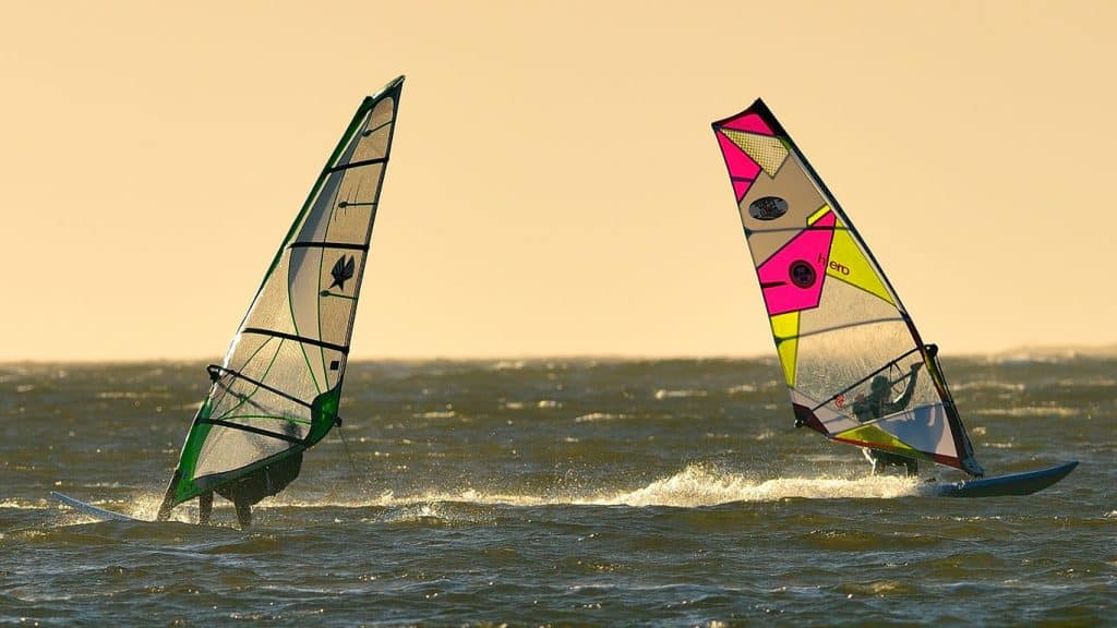 To vindsurfere i fart over vannet med fargerike seil i Ørekroken.