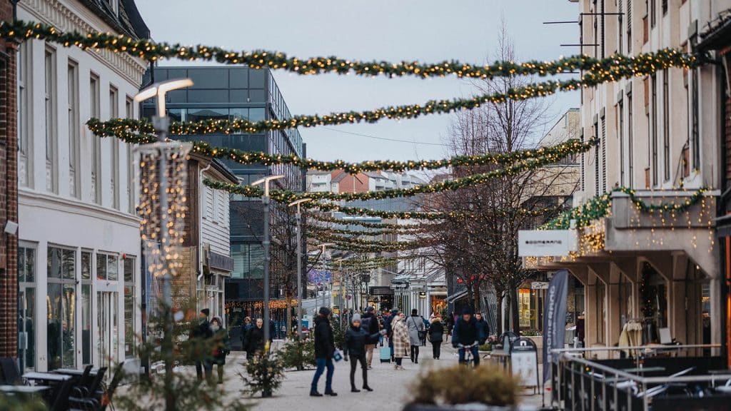 Folk rusler gjennom julepyntet gågate i Fredrikstad sentrum, med lyslenker og granbar over gaten.
