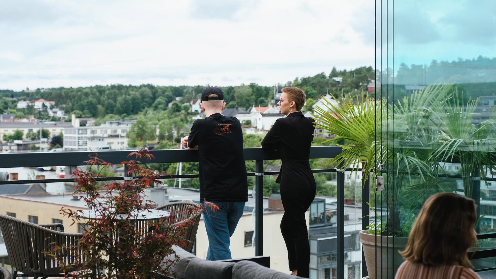 To personer nyter utsikten fra en takterrasse med grønne planter og utsyn over Fredrikstad sentrum.