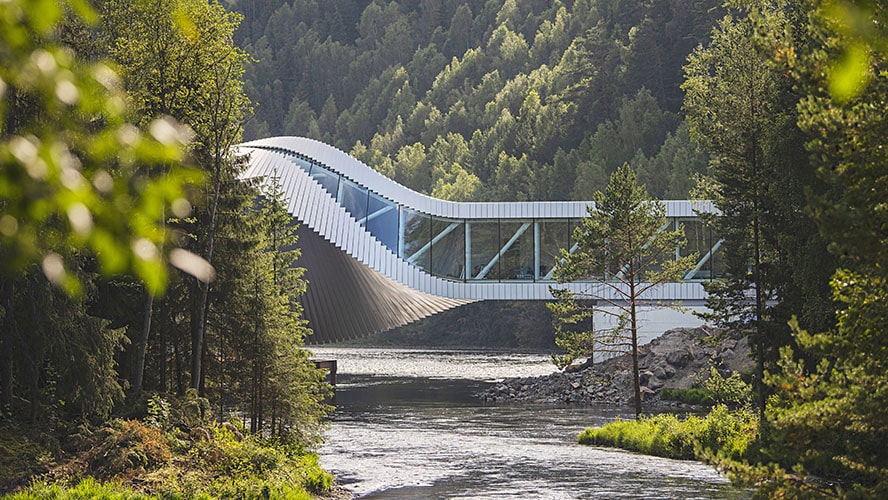 Moderne museumsbygning i form av en vridd bro, The Twist på Kistefos, omgitt av skog og elv.